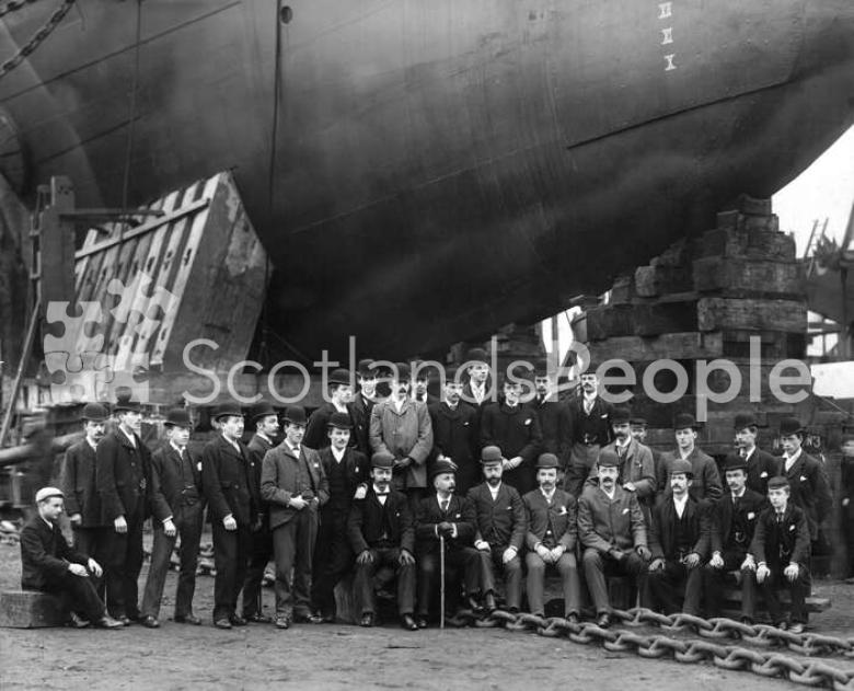 Staff of J & G Thomson posing before the bow of HMS Ramilies on the slip way on the day of the launch.