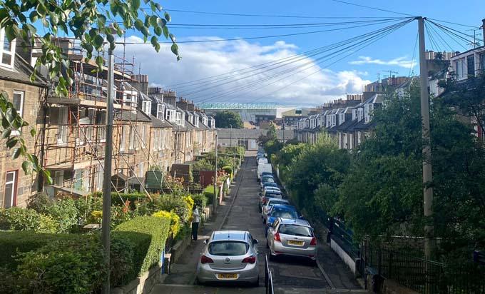 A view of Waverley Place from London Road showing the layout of houses in the colonies. To the left of the photograph are ground level houses. Across the street, hidden behind trees, are staircases which lead to the front door on the first floor. Credit: Crown copyright, National Records of Scotland