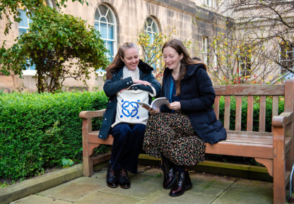 Two people sitting on a bench in the Archivist's Garden at the National Records of Scotland, smiling and looking through a book