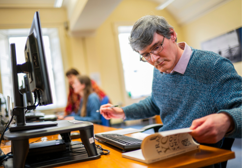 Man leafs through book while sitting at a computer screen in the Scotland's People search room
