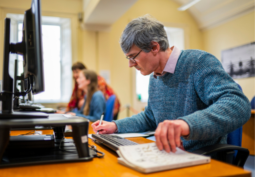 Man writes in a notepad in front of a computer screen in the Scotland's People Centre