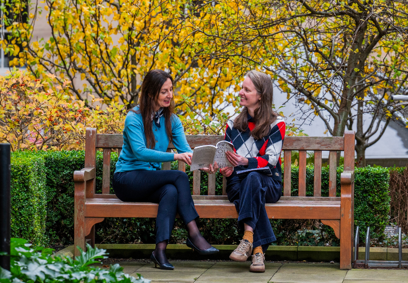 Two women on a bench looking at a book about Scottish ancestors