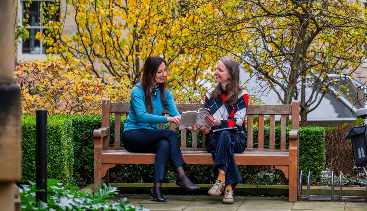 Two women on a bench discussing findings in a book