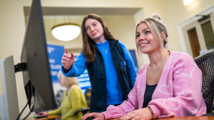Woman smiles looking at a computer screen while another woman points at the screen