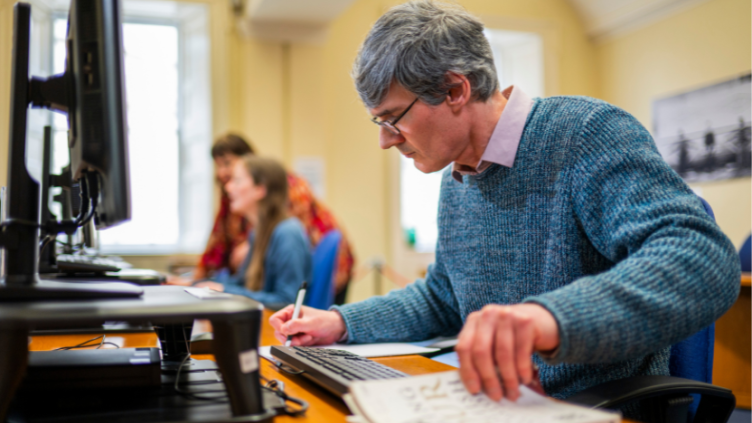 Man writes in a notepad in front of a computer screen in the Scotland's People Centre