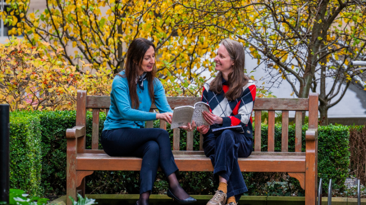 Two women on a bench looking at a book about Scottish ancestors