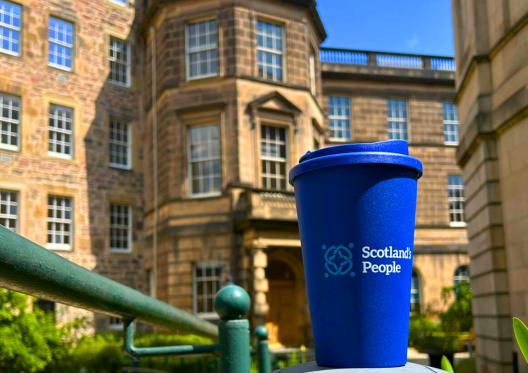 An image of a travel cup with the Scotland's People logo, positioned in a garden